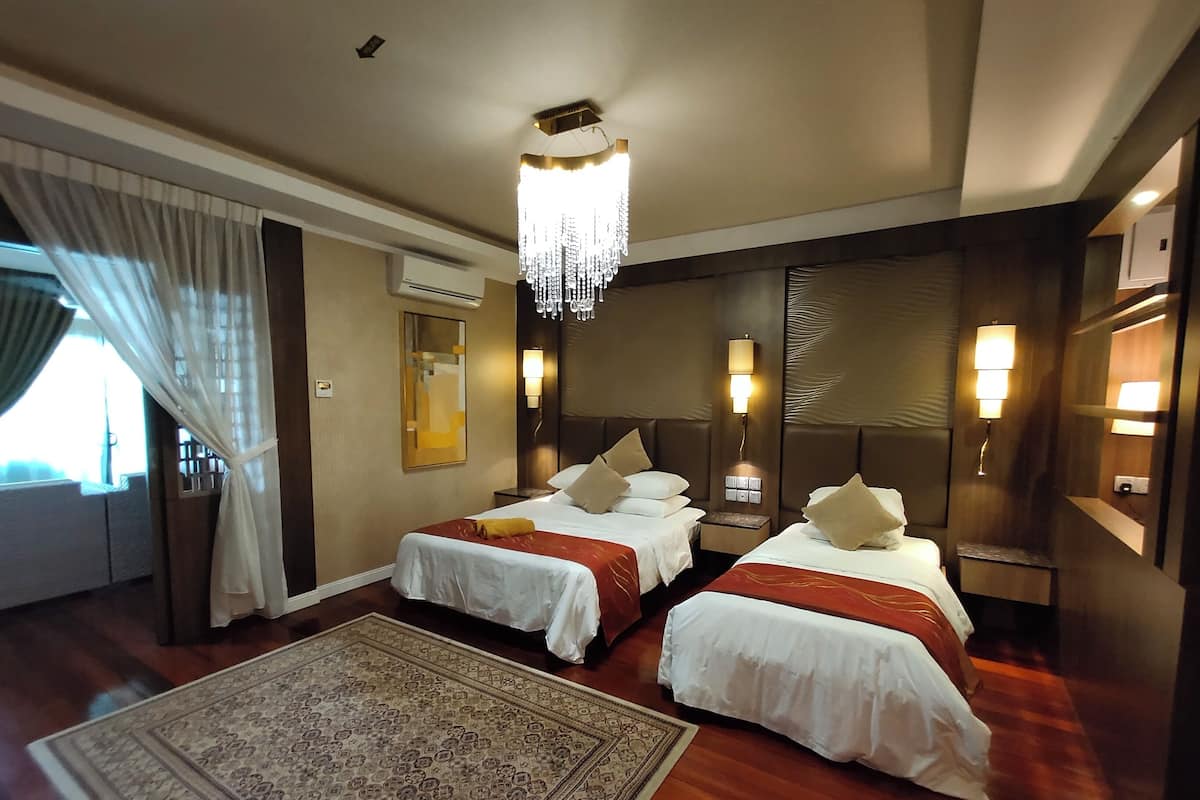 A hotel room with two beds, a large rug, a chandelier, and a view of the outdoors.