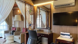 Habitación de hotel con escritorio, silla, televisión y un ventanal grande con cortinas.