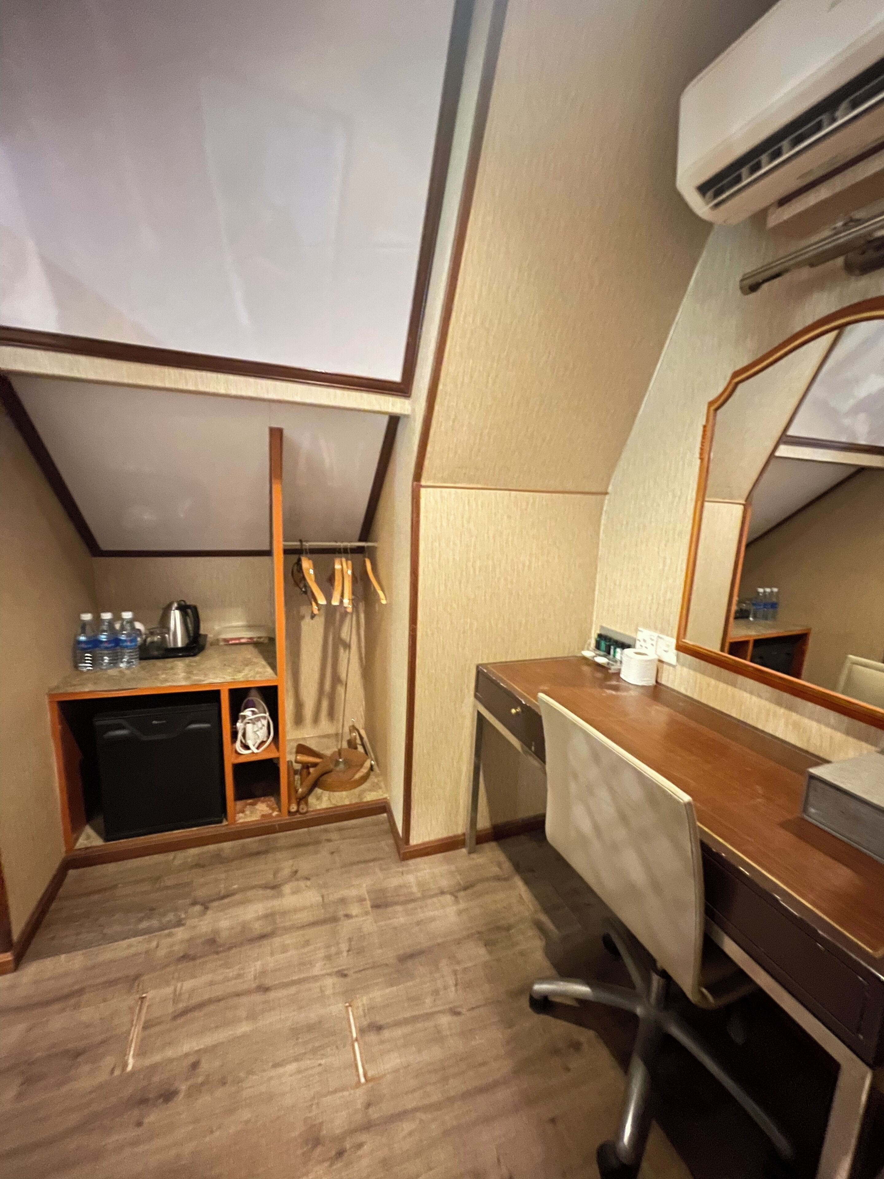 Habitación de hotel compacta con kitchenette, un escritorio pequeño, una silla, un espejo y un ventilador de techo.