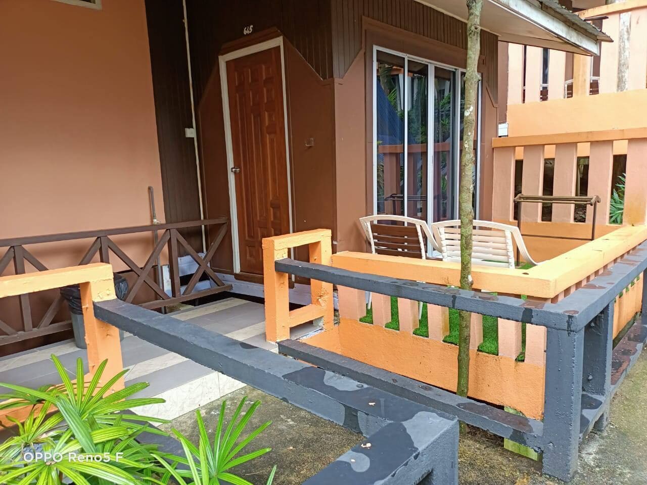 A wooden deck with a bench and a table, a door, and a building with a balcony.