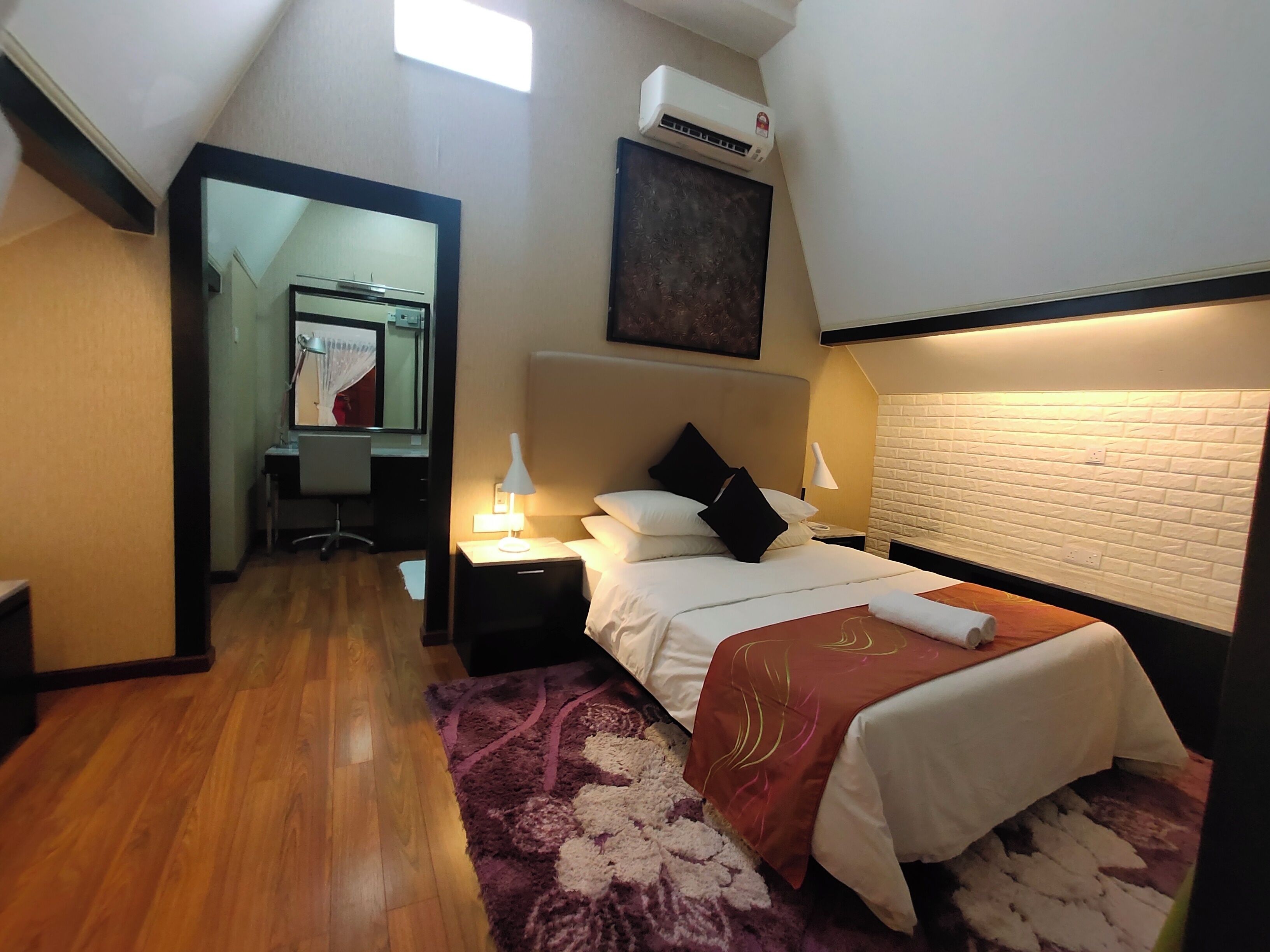 Una habitación de hotel con cama, mesitas de noche, escritorio, silla, espejo y aire acondicionado.