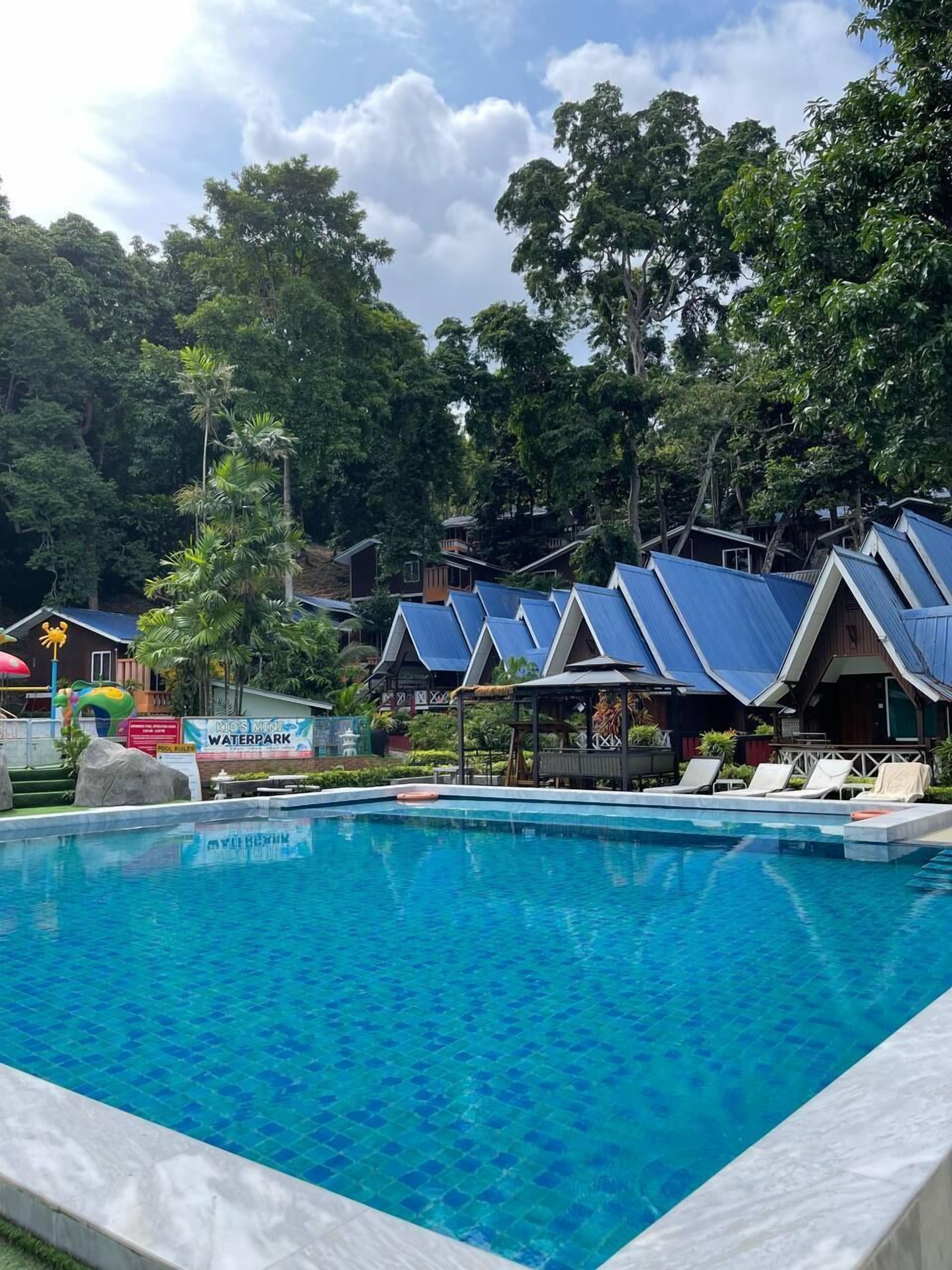 A swimming pool with blue-tiled edges, surrounded by trees and a sign reading "Kids Mini Waterpark".