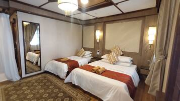 A hotel room with two beds, a large mirror, a patterned rug, and a chandelier.
