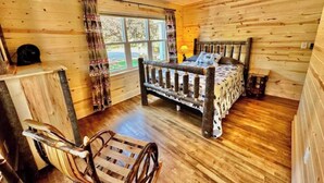 Ein Zimmer in einer Holzhütte mit einem Bett, einem Sessel, einem Deckenventilator und einem Fenster.