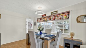 A dining area with a wooden table, grey upholstered chairs, and a decorative banner above the windows. - Lake Okeechobee Fishing Retreat (Okeechobee)