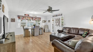 A modern living room with a brown leather sofa, a dining table with chairs, a ceiling fan, and a TV on a stand. - Lake Okeechobee Fishing Retreat (Okeechobee)