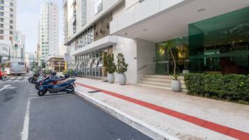 A modern building with a glass facade, a red tactile paving path, and a row of parked motorcycles.