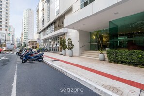 A modern building with a glass facade, a red tactile paving path, and a row of parked motorcycles. - Apto 3 quartos alto padrão em BC - GTR0301 (Balneário Camboriú)