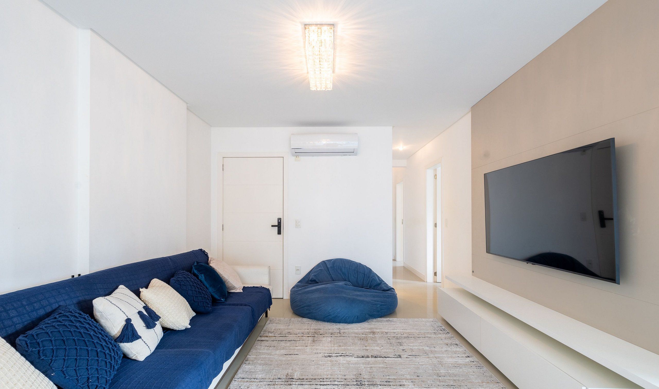 Una sala de estar moderna con un sofá azul, un sillón de saco, un televisor grande y un equipo de aire acondicionado.