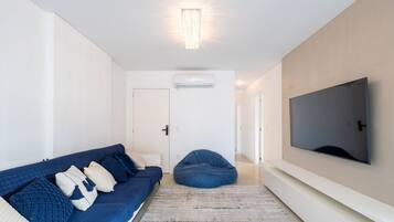 A modern living room with a blue sofa, a bean bag, a large TV, and an air conditioning unit.