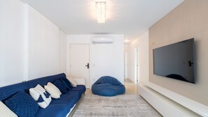 Ein modernes Wohnzimmer mit einem blauen Sofa, einem Sitzsack, einem großen Fernseher und einer Klimaanlage.