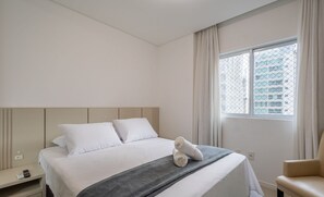 Habitación de hotel con cama, una silla, ventana con cortinas y vista a edificios.