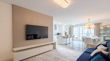 A modern living room with a flat-screen TV, a sofa, and a chandelier.