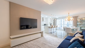 A modern living room with a flat-screen TV, a sofa, and a chandelier. - Apto 3 quartos alto padrão em BC - GTR0301 (Balneário Camboriú)