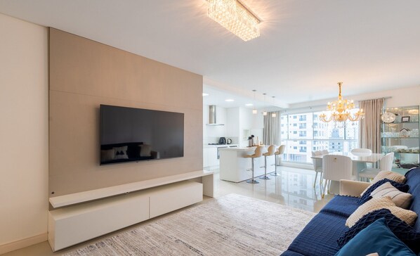 A modern living room with a flat-screen TV, a sofa, and a chandelier. - Apto 3 quartos alto padrão em BC - GTR0301 (Balneário Camboriú)