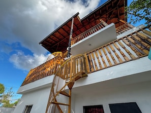 A multi-story building with a wooden balcony, a spiral staircase, and a red roof.