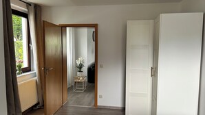 Une chambre à coucher avec un lit, une armoire, une fenêtre avec des rideaux et une petite table sur laquelle est posée une plante.