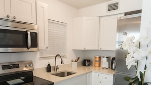 Una cocina moderna con armarios blancos, electrodomésticos de acero inoxidable, un lavamanos y una orquídea decorativa.