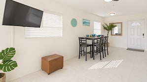 Una sala moderna con televisor de pantalla plana, ventilador de techo, mesa de comedor con sillas y un pequeño reposapiés marrón.