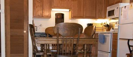 A kitchen with wooden cabinets, a chandelier, a dining table with chairs, and a refrigerator.