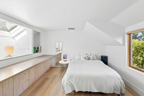 Ein modernes Schlafzimmer mit Oberlicht, einem Bett, einem Nachttisch und einem Fenster mit Blick auf Grünflächen.