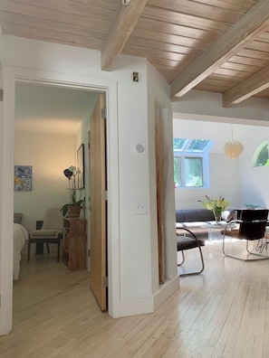A room with wooden flooring, a door leading to another room, a sofa, a chair, and a table with a vase of flowers. - Walking Distance to East Hampton Village, mins to Ocean Beaches (East Hampton)