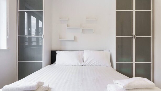 A neatly made bed with white linens and pillows, a black headboard, and two white towels on the side. - Spectacular flat in the heart of Shoreditch (London)