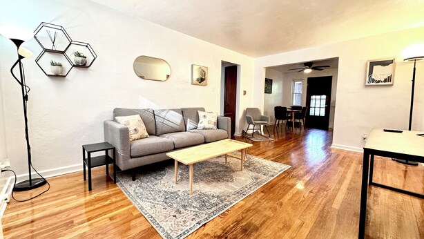 A modern living room with a grey sofa, wooden coffee table, and a patterned rug. There is a dining area with chairs and a table in the background. - Charming 2-bedroom on the West Side! Pet-friendly and quiet! (Cincinnati)