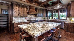 A spacious kitchen with a large granite island, wooden cabinets, and a stone backsplash. - ON CALDERA SPRINGS GOLF COURSE--Spacious 6-bedroom house in enchanting SunRiver! (Bend)