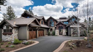 A modern multi-story house with a stone facade, large garage doors, and a curved driveway. - ON CALDERA SPRINGS GOLF COURSE--Spacious 6-bedroom house in enchanting SunRiver! (Bend)