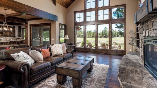 A spacious living room with a large window, a fireplace, and a cozy seating area. - ON CALDERA SPRINGS GOLF COURSE--Spacious 6-bedroom house in enchanting SunRiver! (Bend)