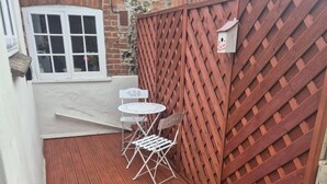 A small outdoor patio with a red wooden deck, a white metal table and chairs, and a red lattice fence.