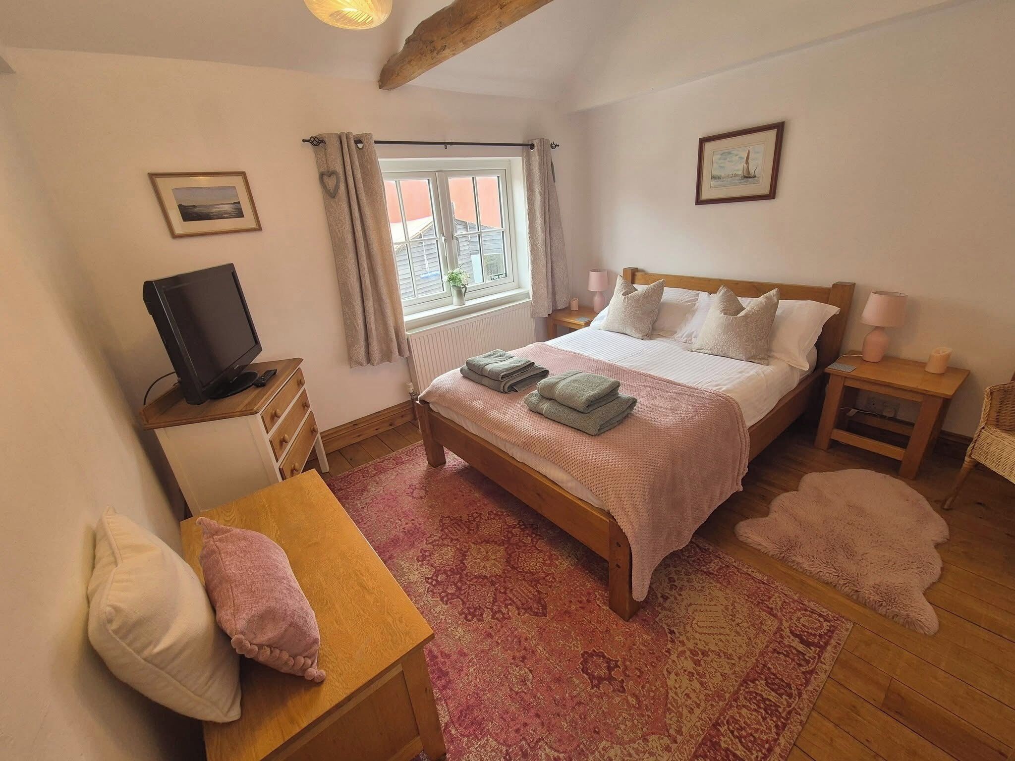 A bedroom with a bed, bedside tables, a television, a window with curtains, and a rug.