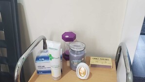 Un baño con ducha, dispensador de jabón, barra de jabón, tarro de vidrio y una caja de cerillas.