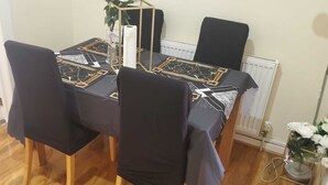 Una mesa de comedor con mantel estampado geométricamente, cuatro sillas negras y un jarrón con flores blancas.
