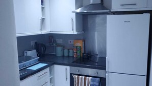 Una cocina compacta con armarios blancos, una campana extractora de acero inoxidable, un refrigerador y una encimera con un hervidor y recipientes.