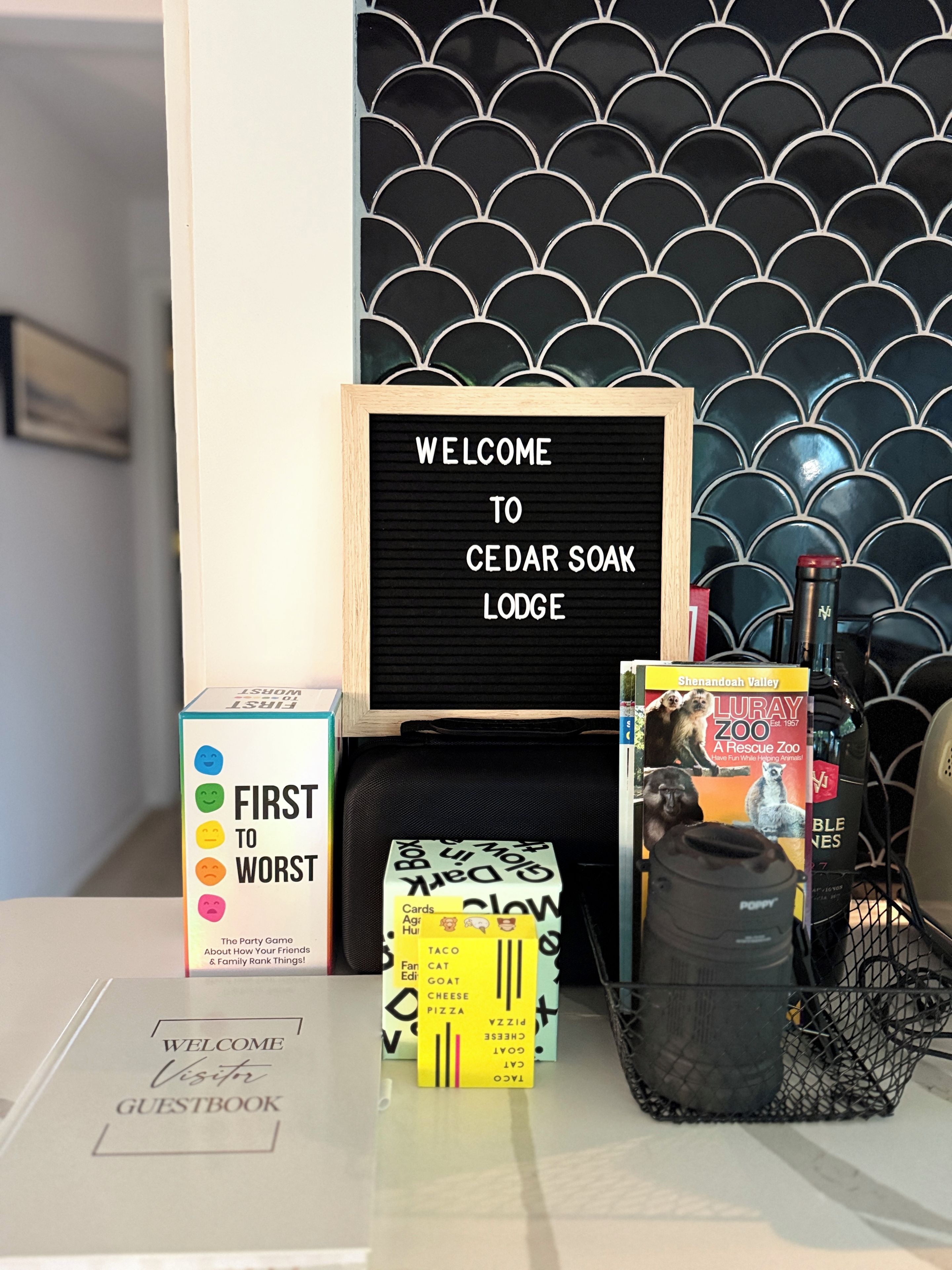 A welcome sign, a guestbook, a game box, and a book on a table with a patterned wall in the background.