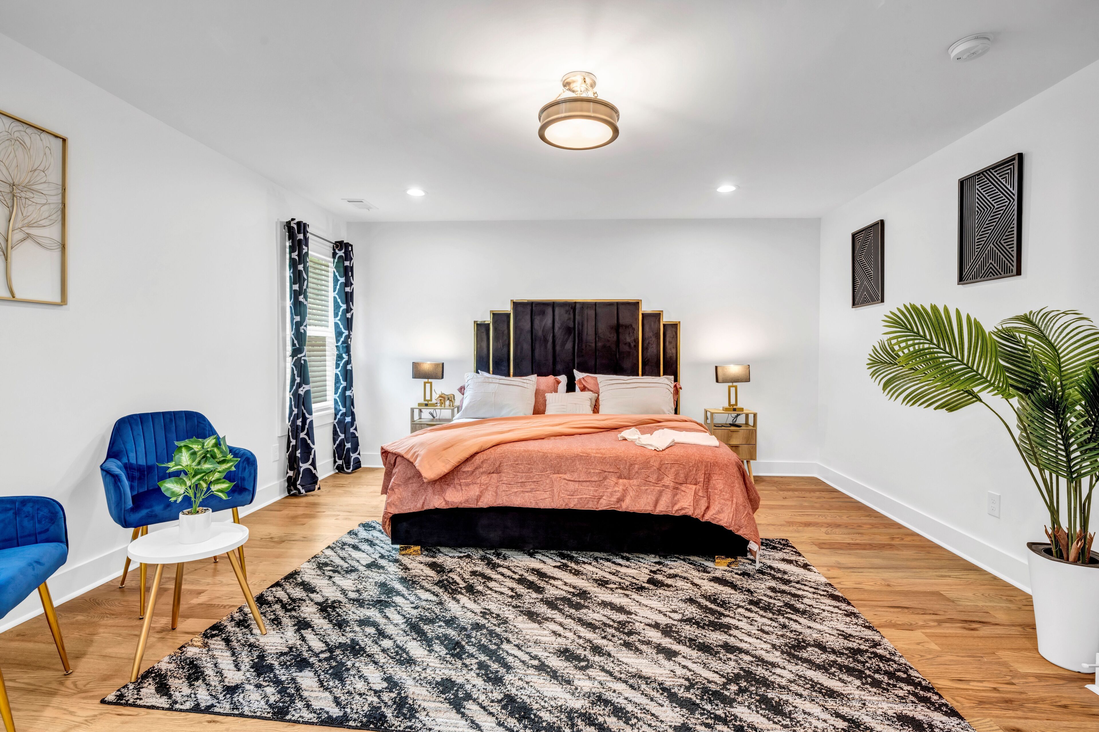 Une chambre moderne avec un grand lit, une chaise bleue, une petite table avec une plante et une grande plante en pot.