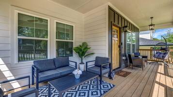 A covered porch with a dark wooden floor, a gray sofa, two armchairs, a coffee table, and a potted plant.