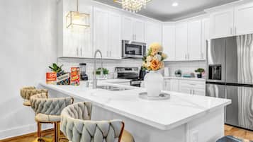 A modern kitchen with white cabinetry, a central island, bar stools, a chandelier, and a stainless steel refrigerator.