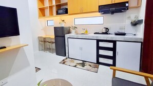 Una cocina moderna con armarios blancos, un refrigerador negro y un microondas integrado. Hay un pequeño comedor con dos sillas y una mesa.