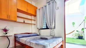 Un dormitorio con cama, armarios de madera, una mesita con una flor y vistas a un jardín.