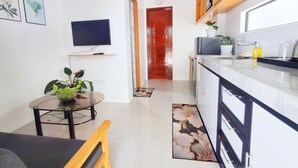 Una cocina moderna con horno empotrado, un lavamanos y una encimera. Hay un comedor con una mesa y sillas, y un televisor montado en la pared.