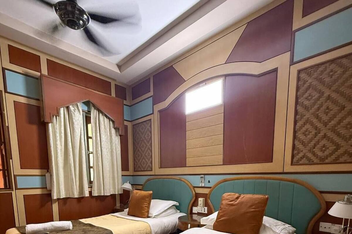 A hotel room with two beds, a ceiling fan, and a window with curtains.