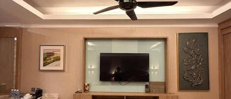 A modern living room with a ceiling fan, a flat-screen TV mounted on a wooden wall, a small round table, and a cabinet with drawers.