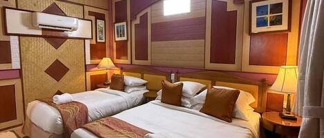 Une chambre d’hôtel avec deux lits, un ventilateur de plafond, un appareil de climatisation et une table de chevet avec une lampe.