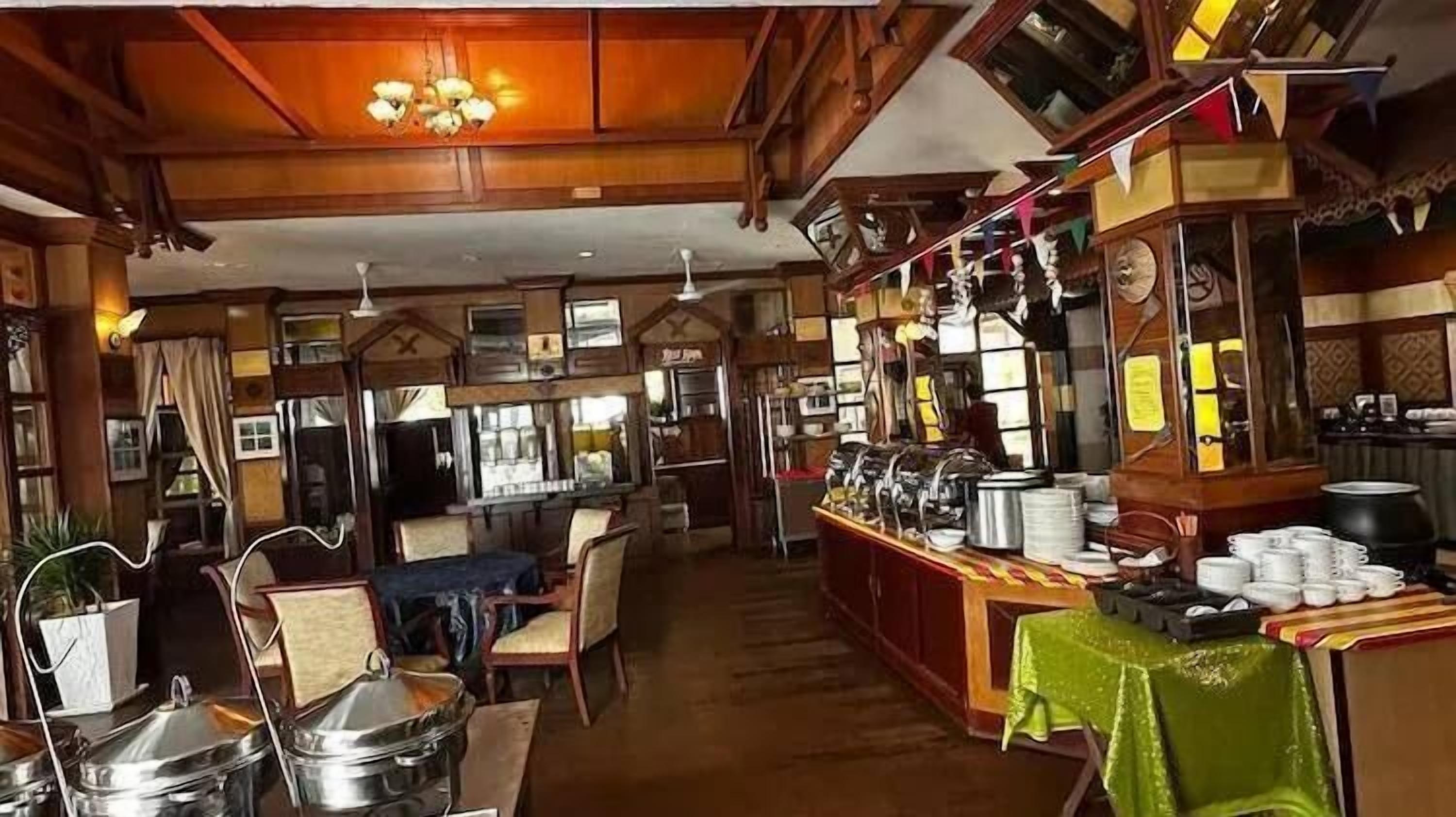 Una posada tradicional con vigas de madera, un área central de comedor con mesas y un rincón de bar con varios utensilios de cocina.