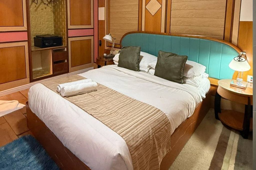 Een netjes opgemaakt bed met een gestreept dekbed, een houten hoofdbord en een nachtkastje met een lamp.