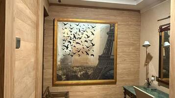 A room with a wooden floor, a desk with a chair, a lamp, and a framed picture of the Eiffel Tower with birds flying in the foreground.
