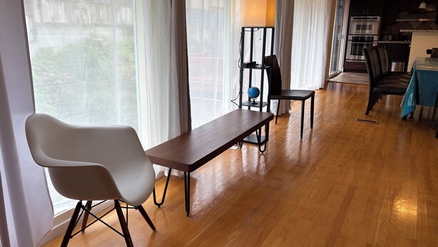 Una sala de estar moderna con piso de madera, una mesa de comedor con sillas, una lámpara de pie y vistas amplias por las ventanas.
